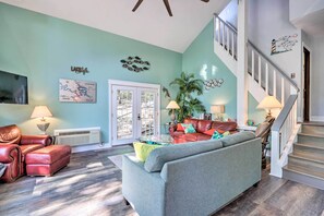 A living room with a sofa, a red leather chair, a coffee table, and a staircase leading to the upper floor. - 2 Mi to Margaritaville: Lake of the Ozarks Home! (Osage Beach)