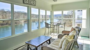 Ein Wintergarten mit Blick auf einen Fluss, mit Korbmöbeln, einem Tisch und einem Deckenventilator.