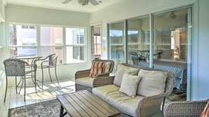 Eine sonnendurchflutete Terrasse mit Korbmöbeln, einem Deckenventilator und großen Schiebeglastüren, die zu einem Außenbereich führen.