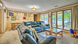 A spacious living room with a leather sofa, a wooden coffee table, and a dining table. Large windows provide a view of the outdoors. - Boat Dock + Slides: Lakefront Gravois Mills Home (Gravois Mills)