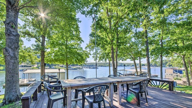A wooden deck with a table and chairs overlooking a lake, surrounded by trees. - Boat Dock + Slides: Lakefront Gravois Mills Home (Gravois Mills)