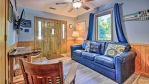 A cozy living room with a blue leather sofa, wooden dining table, and a ceiling fan. - Boat Dock + Slides: Lakefront Gravois Mills Home (Gravois Mills)