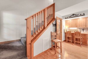 A staircase with wooden railings leading to a kitchen area with wooden cabinets and a bar counter.