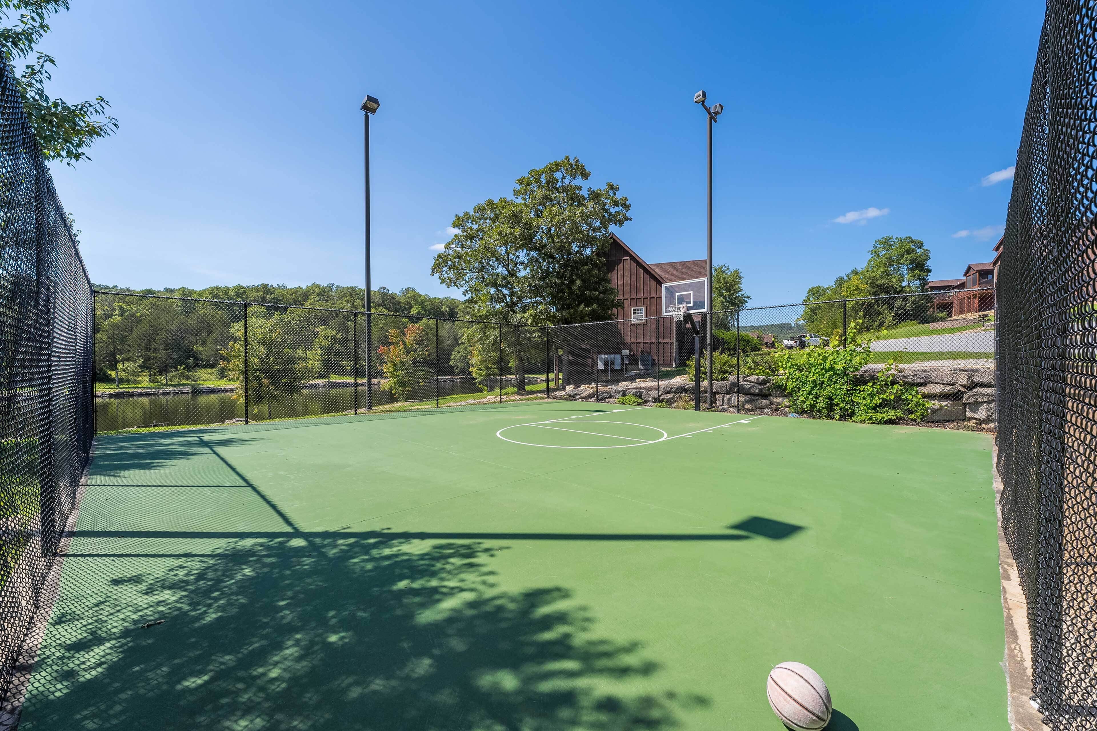 Ein Basketballplatz im Freien mit grüner Spielfläche, umgeben von einem Maschendrahtzaun.
