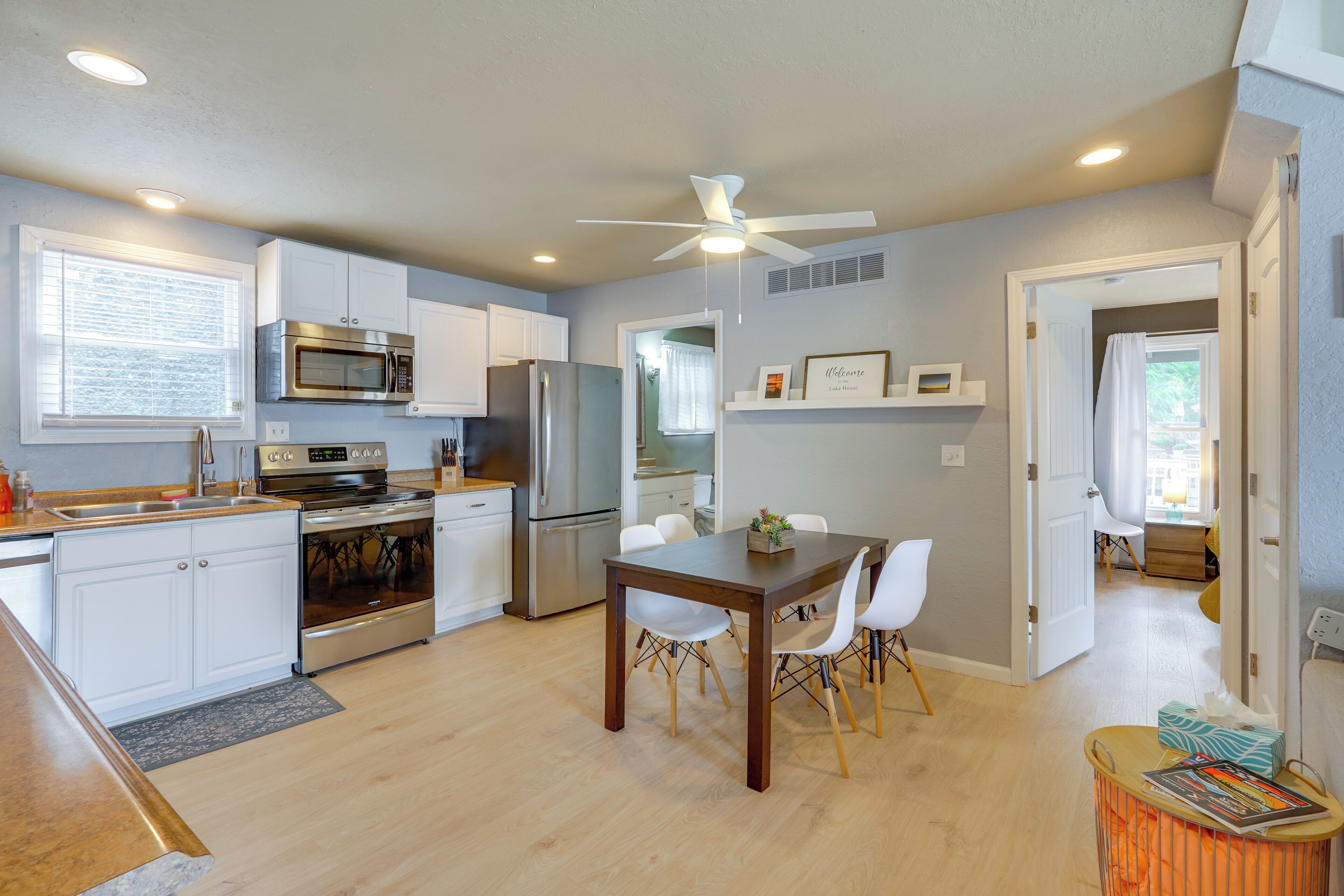 A modern kitchen with white cabinetry, stainless steel appliances, and a dining area with a wooden table and white chairs.