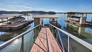 Un muelle de madera que conduce a un embarcadero con zonas de estar cubiertas y un pequeño refugio.