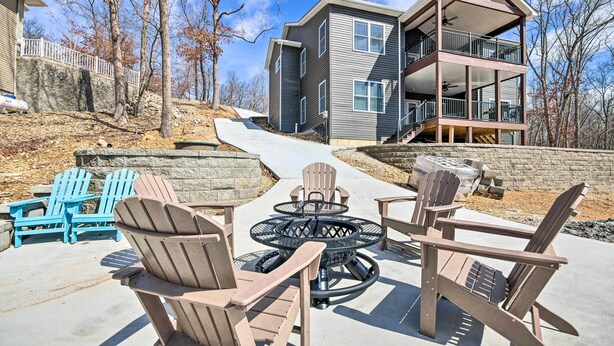 Une maison à deux étages dotée d’un balcon, d’un espace extérieur aménagé avec des fauteuils Adirondack et d’un foyer.