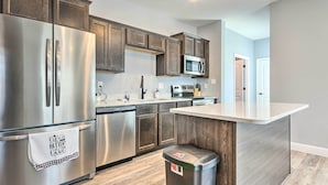 Une cuisine moderne dotée d’appareils électroménagers en acier inoxydable, de meubles en bois et d’un plan de travail blanc.