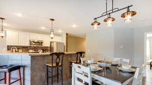 Cozinha moderna com armários brancos, eletrodomésticos de aço inoxidável e um espaço de jantar com cadeiras brancas e uma mesa escura.