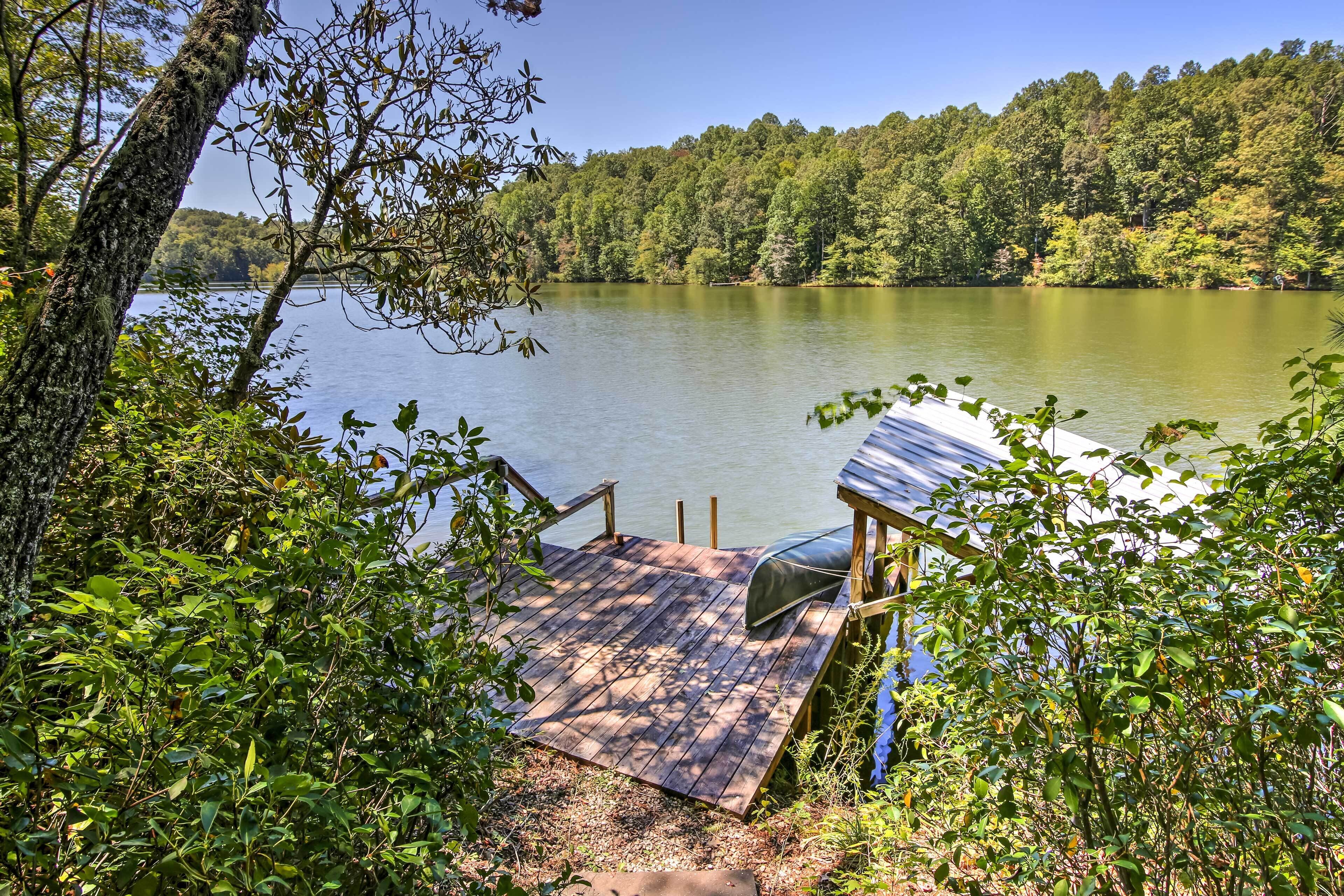 A wooden deck leading to a lake with a covered seating area and a view of a forested hillside.