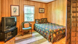 Una habitación con paneles de madera, una cama, una silla, un televisor y una ventana.