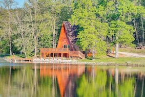 A cabin with a triangular roof, wooden deck, and a dock extending into a lake, surrounded by trees. - Lakefront A-frame Cabin With Community Perks (Columbia)