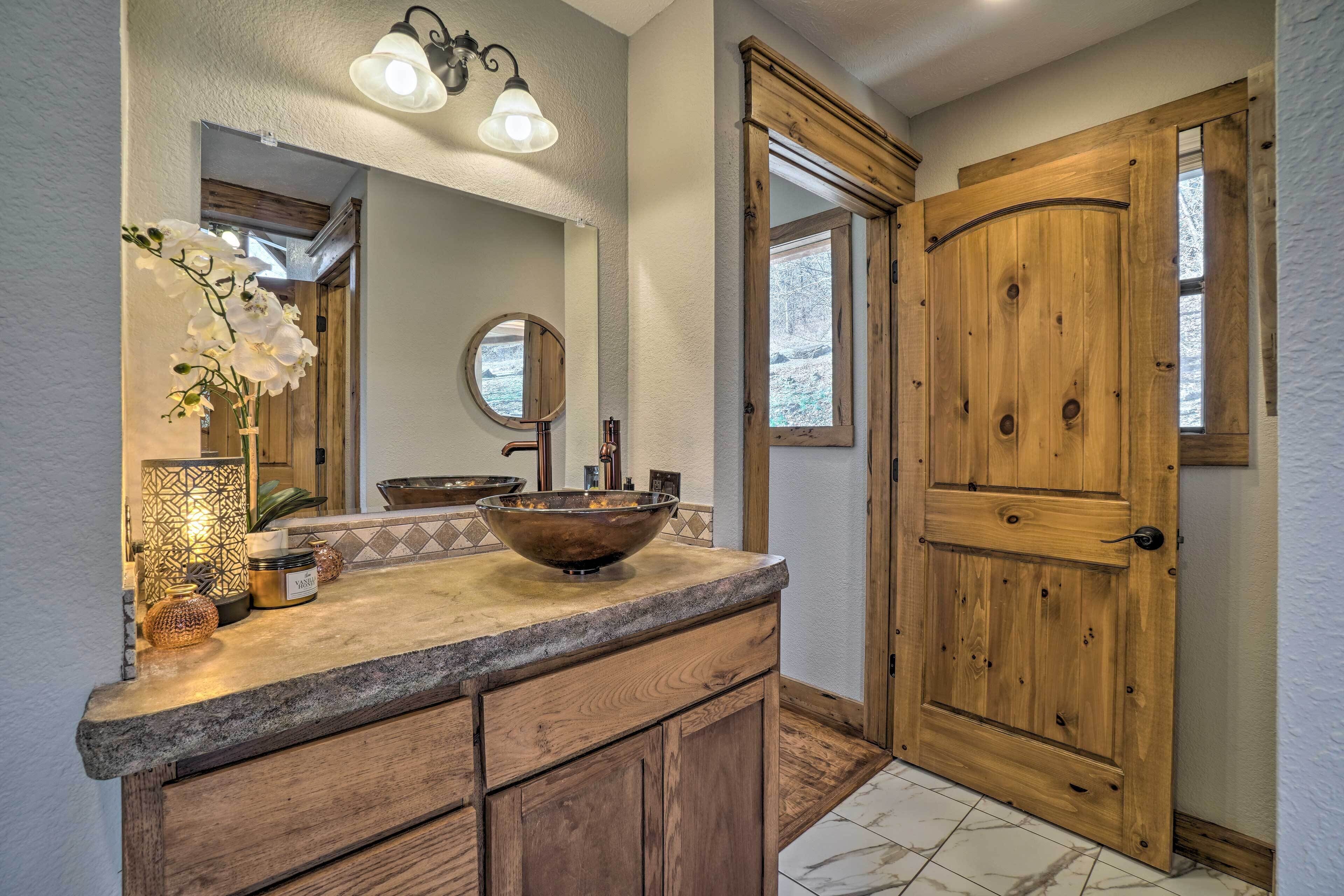 A bathroom with a large wooden door, a round mirror, a vessel sink, and a light fixture above the mirror.