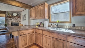 A kitchen with wooden cabinets, a stone fireplace, and a large window. - Lakefront Shell Knob Home w/ Deck & Gas Grill (Shell Knob)