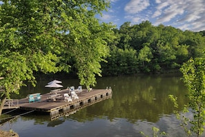 A dock with chairs and tables, surrounded by lush greenery and a calm lake.