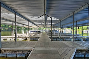 A covered dock area with multiple mooring points, a central walkway, and a view of boats and greenery in the background.