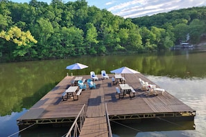A wooden dock with lounge chairs and umbrellas, surrounded by a forested area.