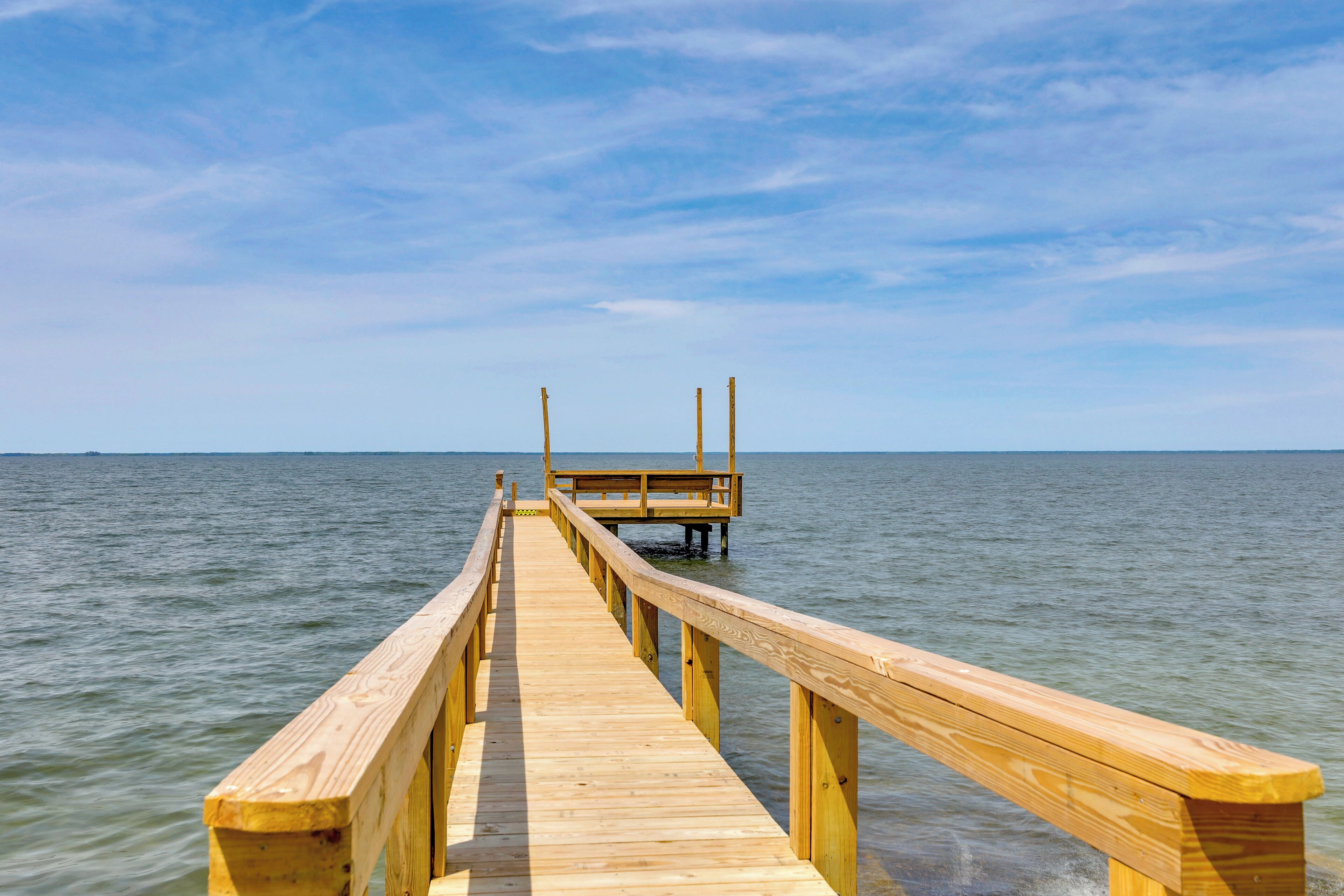 A wooden pier extending into calm water with a clear sky above.