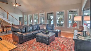 A spacious living room with a large sectional sofa, a coffee table, and a patterned rug. There are multiple windows providing natural light and a view of the outdoors. - Lakefront Retreat w/ Game Room & Private Dock! (Bonneau)