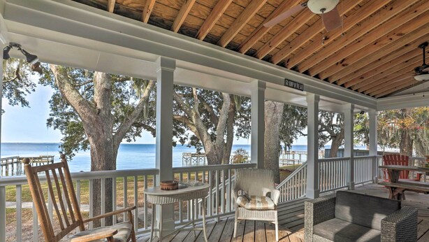 A covered outdoor deck with wicker furniture, a table, and a view of the ocean. - Lakefront Retreat w/ Game Room & Private Dock! (Bonneau)