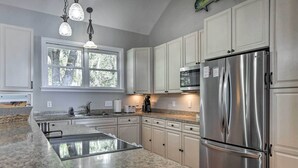 A modern kitchen with granite countertops, stainless steel appliances, white cabinetry, and a large window providing natural light. - Lakefront Retreat w/ Game Room & Private Dock! (Bonneau)