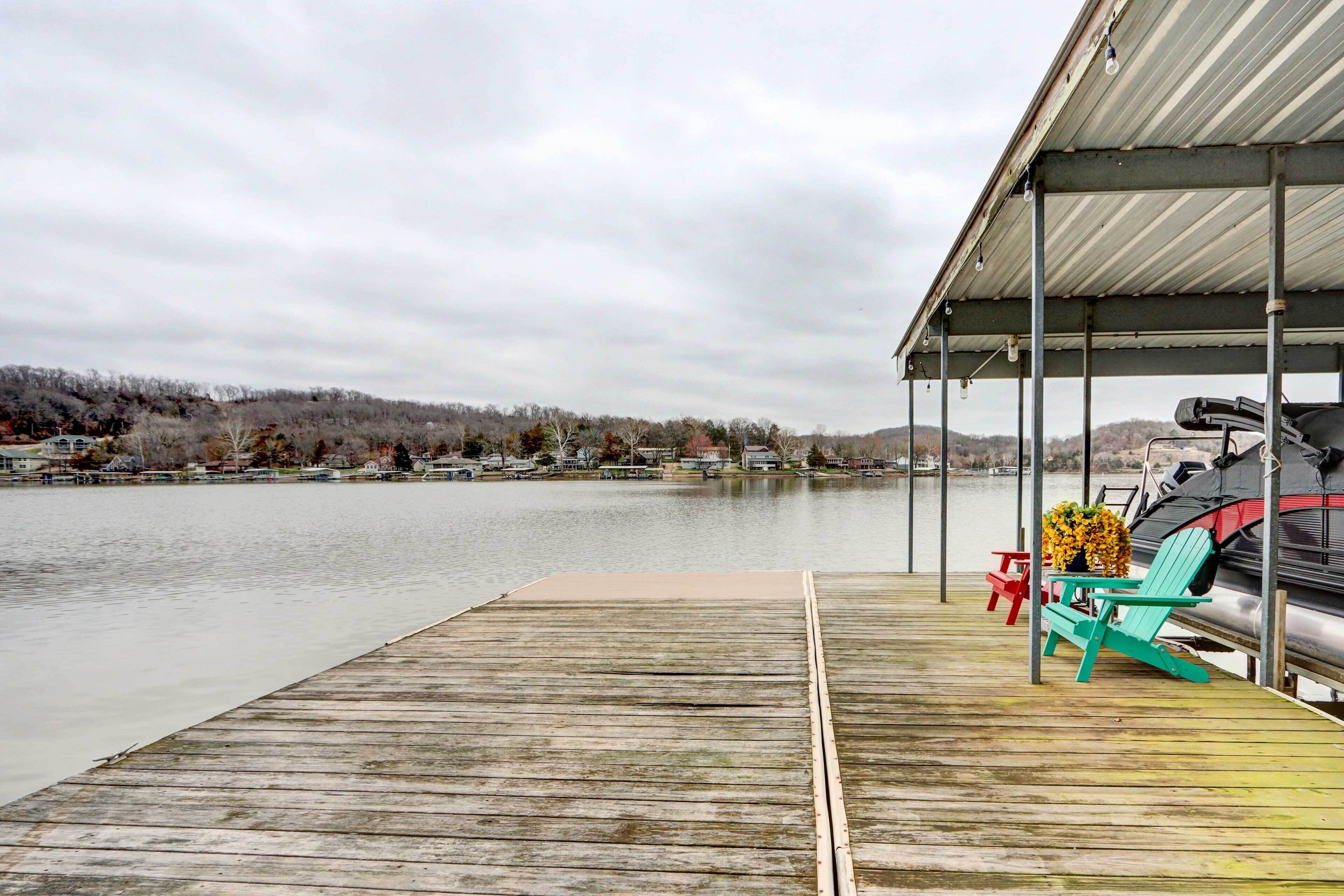 A wooden dock extending into a calm lake with a covered area featuring a grill and outdoor seating.