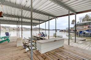 A covered dock with chairs and a cooler, overlooking a calm body of water with boats in the background.
