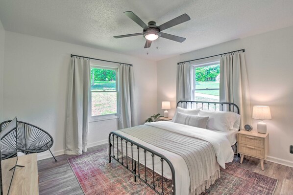 A bedroom with a bed, bedside tables, a ceiling fan, and windows with curtains. - Tranquil Townville Gem With Kayaks (Townville)