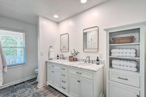 A bathroom with white cabinetry, a marble countertop, a sink, a mirror, a window with blinds, and a towel rack. - Tranquil Townville Gem With Kayaks (Townville)