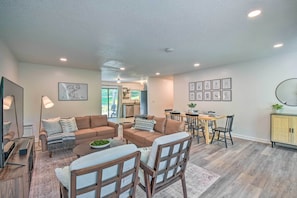 A modern living room with a sofa set, a dining table, and chairs. There is a kitchen area in the background.