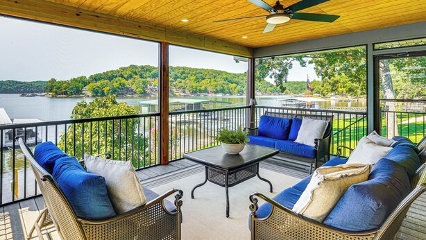 A balcony with wicker furniture, a table with a plant, and a view of a lake and hills. - Dock & Water Slide: Family Lake of the Ozarks Home (Gravois Mills)