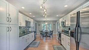Una cocina moderna con armarios blancos, electrodomésticos de acero inoxidable y un comedor con candelabro.