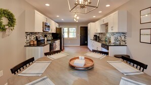 Una cocina moderna con armarios blancos, una isla central con una bandeja y una zona de comedor con una mesa y sillas de madera.