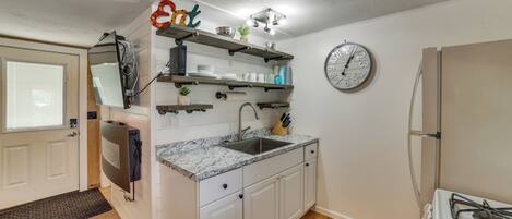 Une cuisine avec des armoires blanches, un comptoir en granit, un évier en acier inoxydable et une horloge au mur.