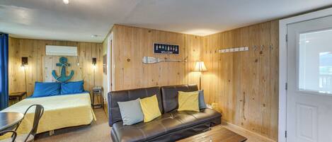 A room with a bed, a sofa, a coffee table, a lamp, a wall-mounted sign, and a door.
