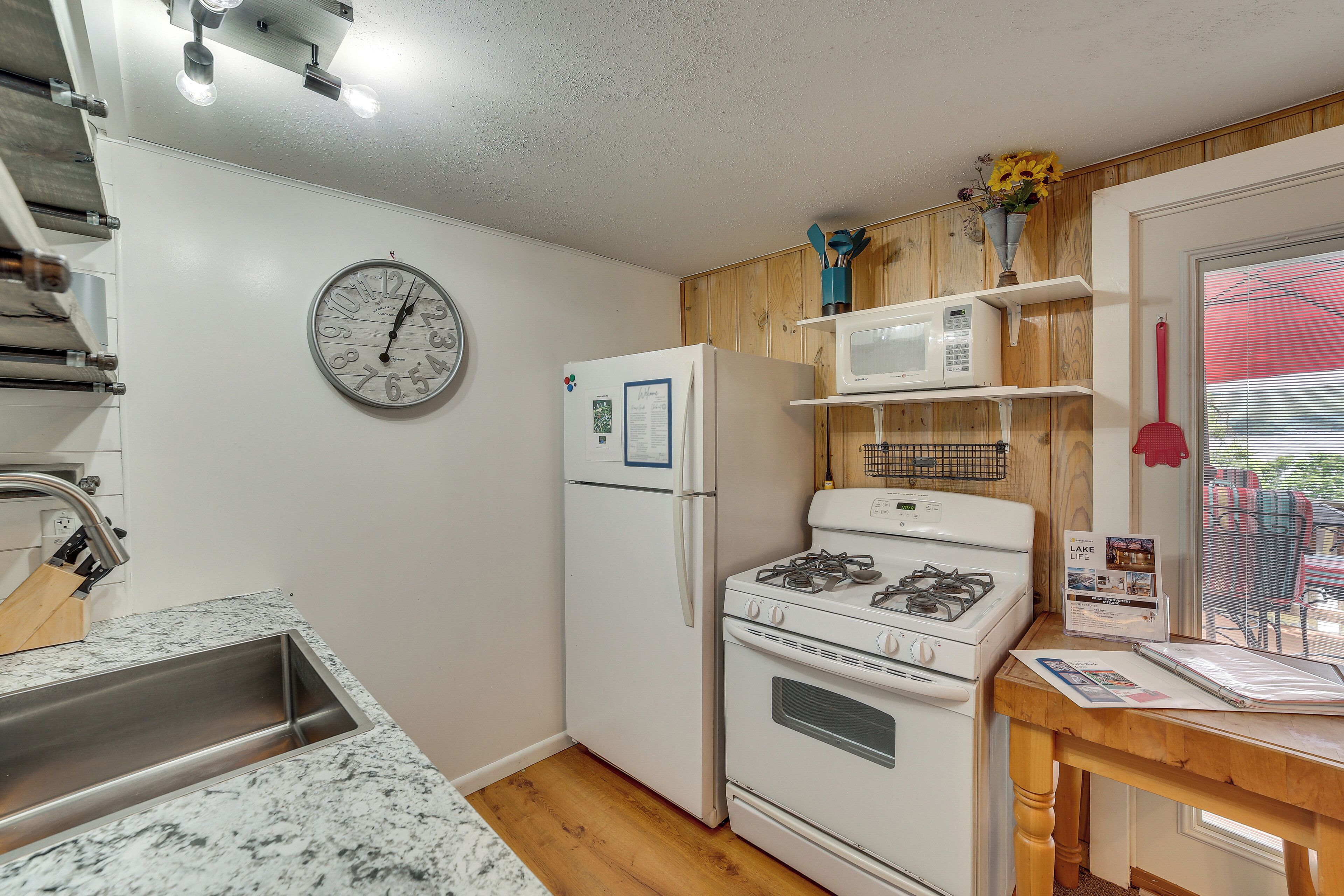 Cocina compacta con refrigerador, estufa, microondas y un reloj en la pared.