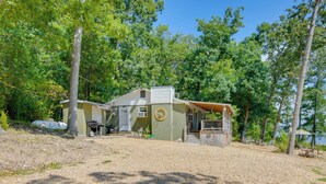 Une cabane à deux étages avec un porche couvert, une petite terrasse et une allée gravillonnée.
