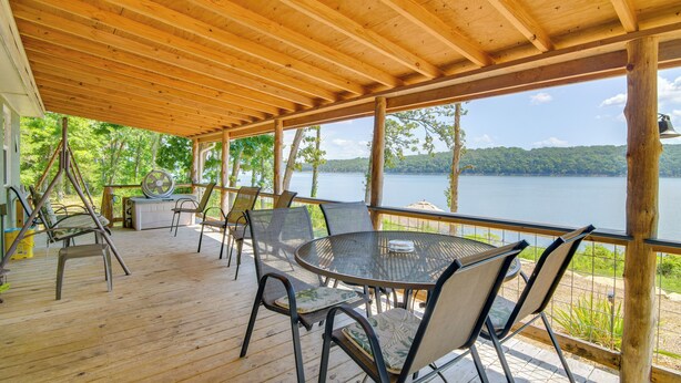 Une terrasse extérieure couverte avec un plafond en bois, une table ronde avec des chaises et une vue sur un lac.