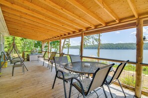 Una terraza techada al aire libre con techo de madera, una mesa redonda con sillas y vistas a un lago.