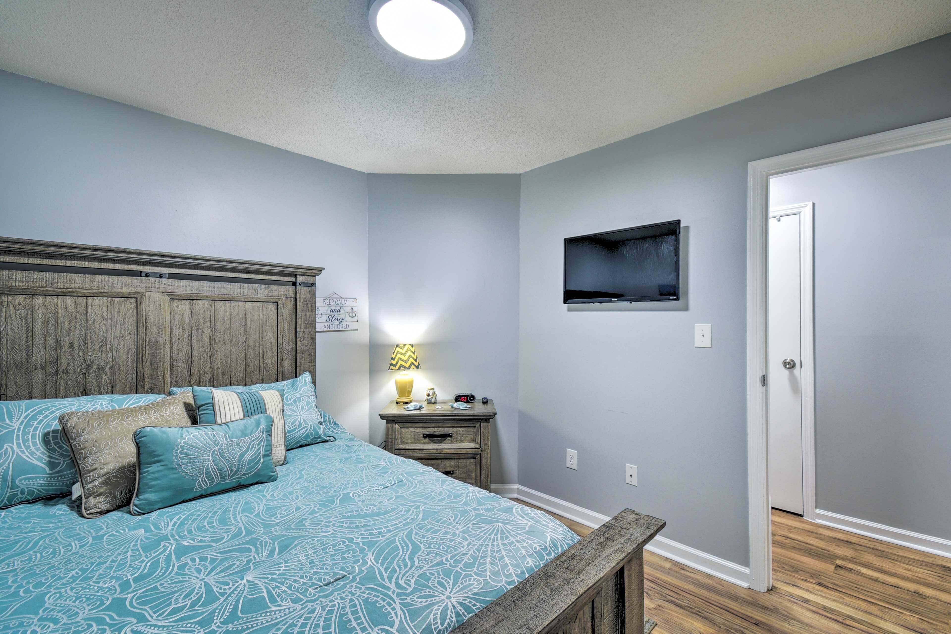 A bedroom with a bed, a nightstand, a TV mounted on the wall, and a door.