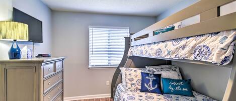 A bedroom with a bunk bed, a dresser, a lamp, and a window with blinds.