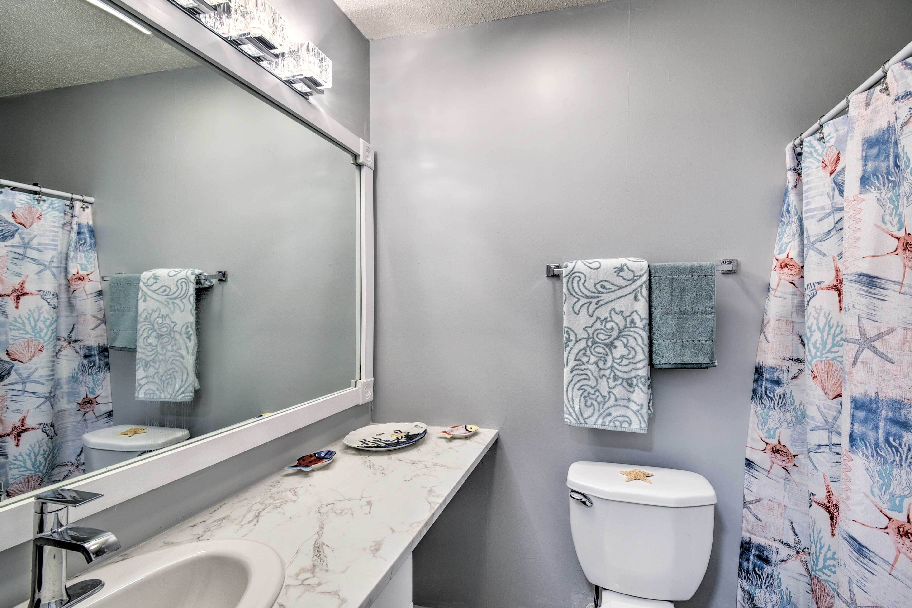 Un baño con lavamanos de mármol, inodoro decorado con una estrella de mar y cortina de ducha con motivos marinos.