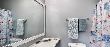 Un baño con lavamanos de mármol, inodoro decorado con una estrella de mar y cortina de ducha con motivos marinos.