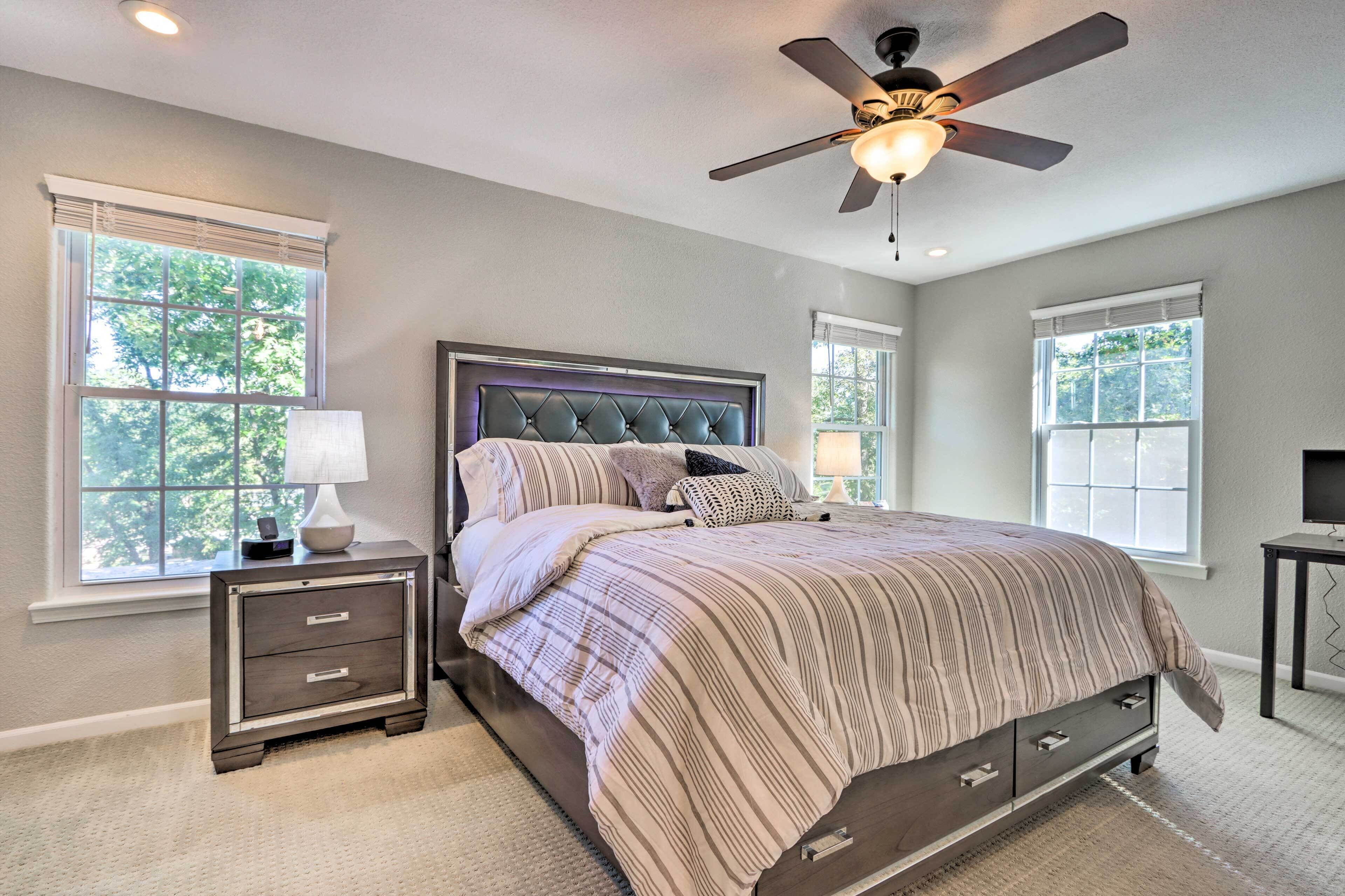 A bedroom with a bed, nightstands, a ceiling fan, and windows.
