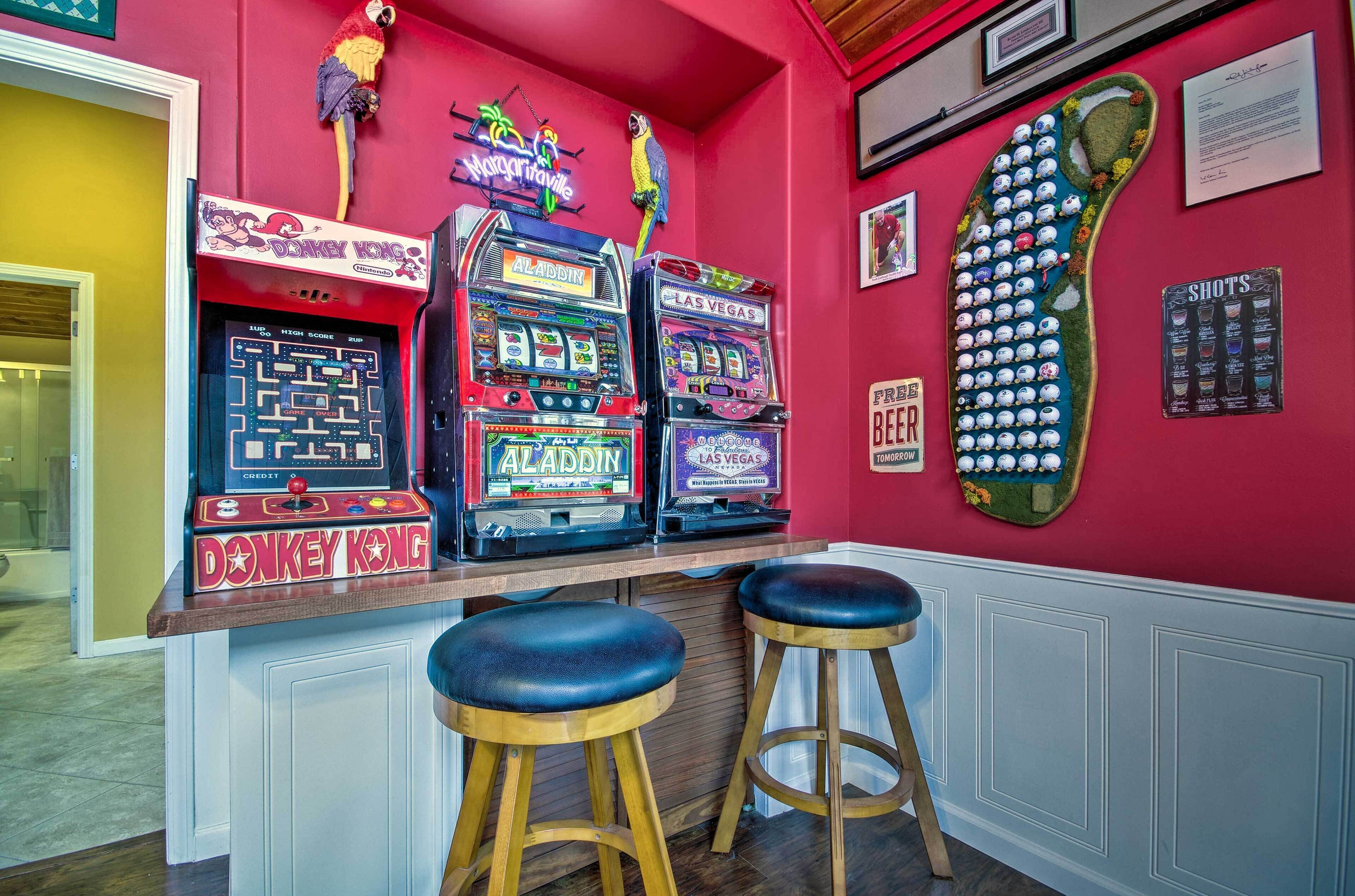 A bar area with arcade games, stools, and a neon sign.