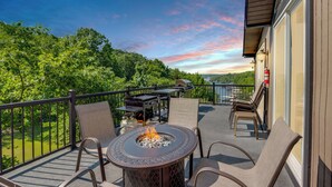 Ein Balkon mit Feuertisch, Gartenmöbeln und einem schönen Blick auf Bäume und Hügel.