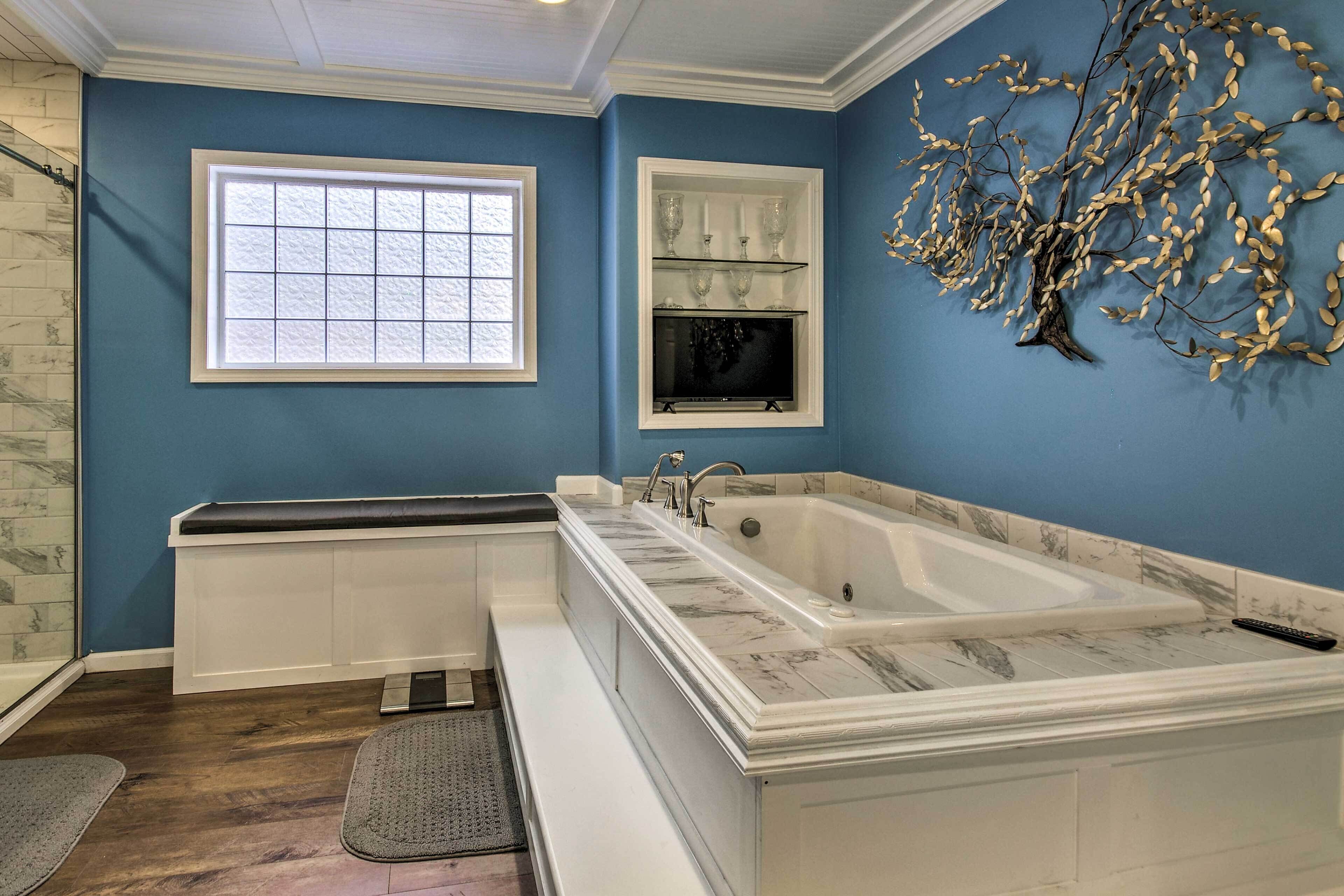 Une salle de bain dotée d’une grande baignoire, d’une fenêtre et d’une étagère murale où sont rangés des objets en verre.