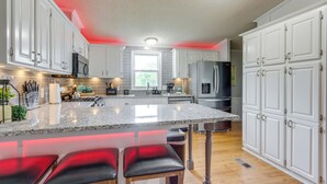 A modern kitchen with white cabinets, a granite countertop, and a central island with bar stools. - 8 Mi to Beach: Lake-view Haven in Linn Creek! (Linn Creek)