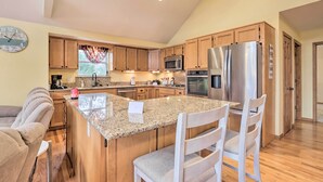 A modern kitchen with granite countertops, stainless steel appliances, wooden cabinets, and a large island with bar stools. - 'lazy RS Lakehouse' w/ Hot Tub & Dock in Warsaw! (Warsaw)