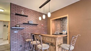A kitchen with a brick wall, wooden bar counter, and three bar stools. - 'lazy RS Lakehouse' w/ Hot Tub & Dock in Warsaw! (Warsaw)